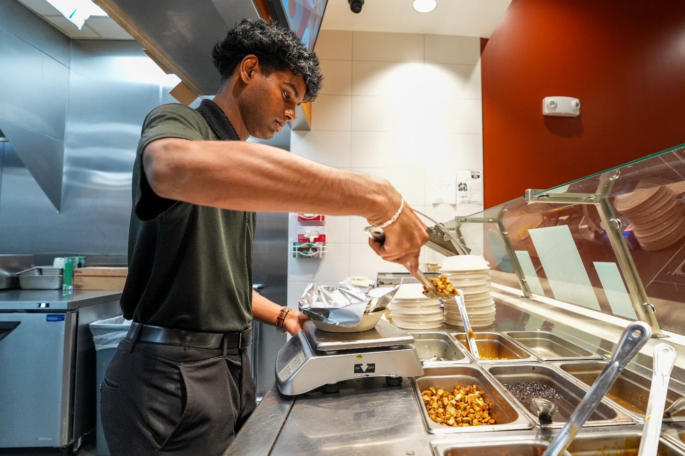Sai Vajaha tonging chicken from the line into a bowl that sits on a kitchen scale